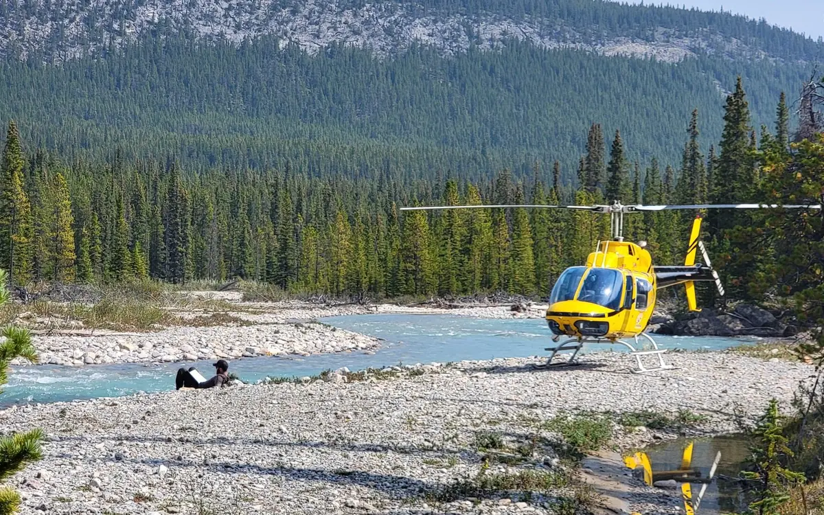 A helicopter landed beside a river in the Canadian Rockies