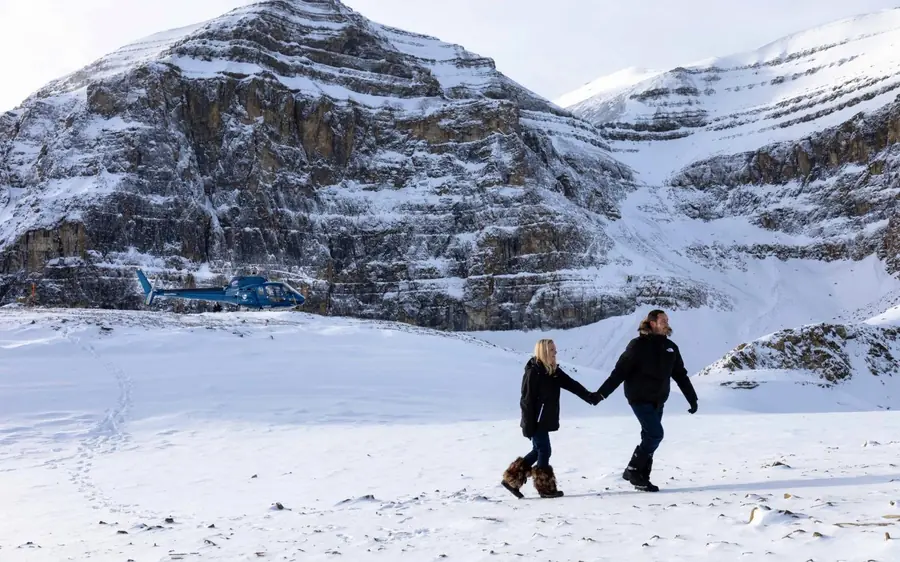 A couple walking in snow beside a helicopter in the Rockies